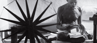 Mahatma Gandhi leyendo al lado de su máquina de tejer.