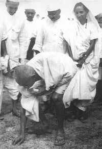 Gandhi en Dandi, Gujarat del Sur, recogiendo sal en la playa al final de la Marcha de la Sal, 5 de abril de 1930. Detrás de él está su segundo hijo Manilal Gandhi y Mithuben Petit. Autor desconocido - http://www.calpeacepower.org/0101/images/1930-pick-salt-GS_BG.jpg, Dominio Público, https://commons.wikimedia.org/w/index.php?curid=2082661